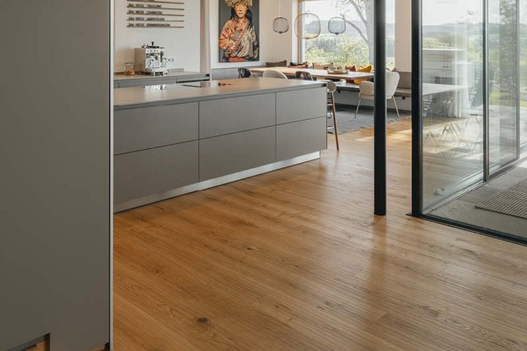 Kitchen in gray with large glass fronts with a view of nature. You can also see a high-quality oak parquet floor laid across the entire room