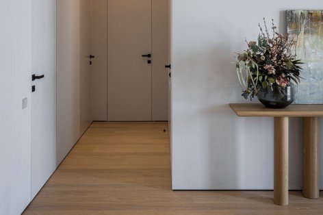 Wohnbereich mit hellen Landhausdielen aus Eiche und mehreren modernen weißen Türen. An der Wand steht ein schmaler Konsolentisch, darauf ein Blumenstrauß als Dekoration.