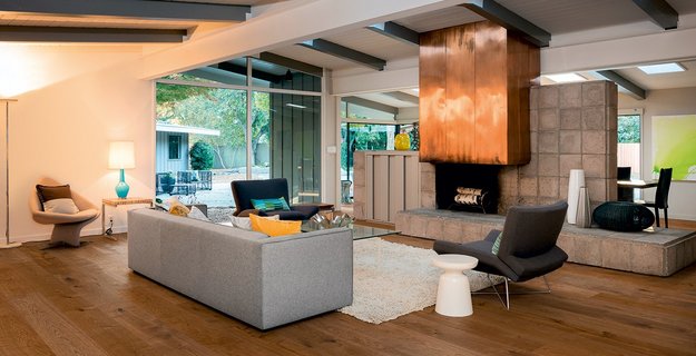 Wohnzimmer mit hochwertigem Eichenholz-Parkettboden in warmem Braunton, der Raum straht eine gemütliche, herbstliche Stimmung aus und verfügt über einen großen offenen Kupferkamin und moderne Möbel in grau.