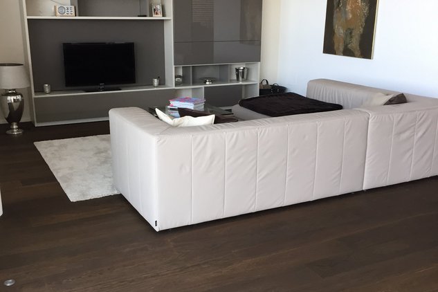 Dunkles Eichenparkett mit heller Couch und grauer Wohnwand