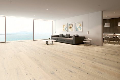 Weitläufiges Wohnzimmer mit Eichenparkett rustikal weiß, grauem Sofa und Fensterfront mit Meerblick.