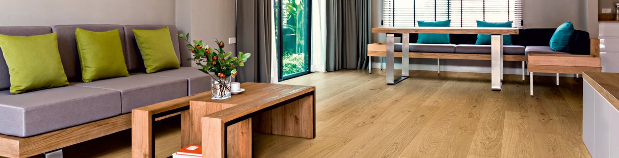 Ländliches Wohnzimmer mit Holzmöbeln und Landhausdiele aus Eiche. Auf den Sitzgelegenheiten befinden sich bunte Polster.
