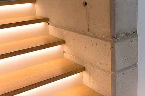 Detailed view of an illuminated wooden staircase with integrated LED strips next to an exposed concrete wall
