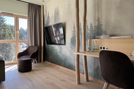 Helles Hotelzimmer mit Neumaterialien, Waldtapete und Eichenparkett.