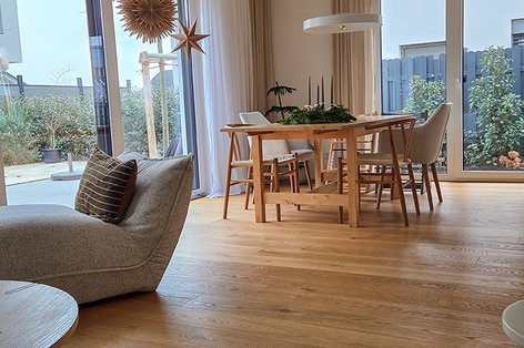 Esszimmer mit bodentiefen Fenstern und Landhausdiele Eiche, Holztisch und Sesseln aus hellem Stoff.