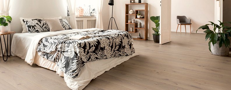 [Translate to EN:] Schlafzimmer mit floraler Überdecke, schwarzer Stehlampe und grauem Holzboden