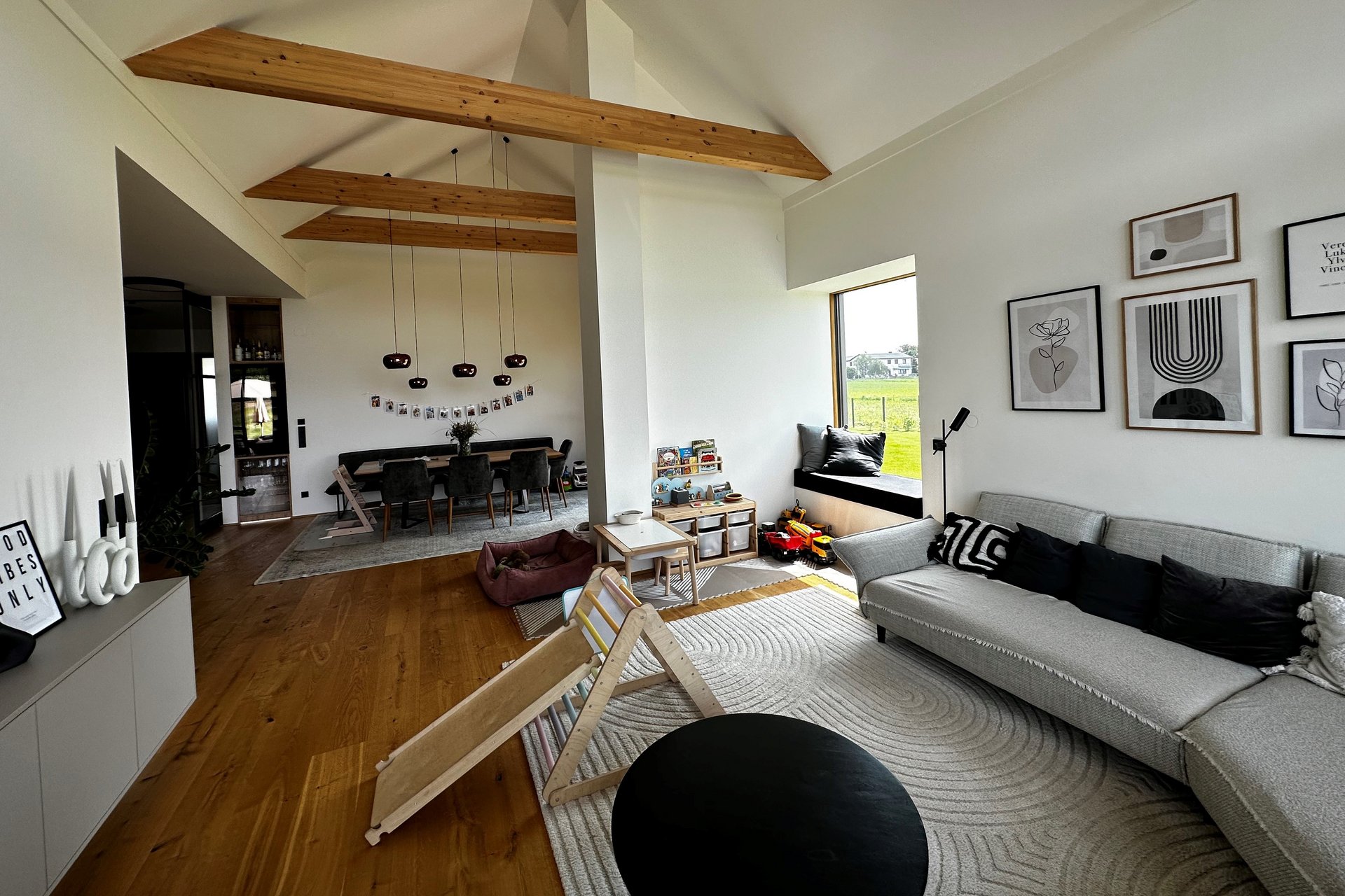 Graues Sofa auf naturfarbenem Teppich in offenem Wohnraum mit Holzbalken und Parkett