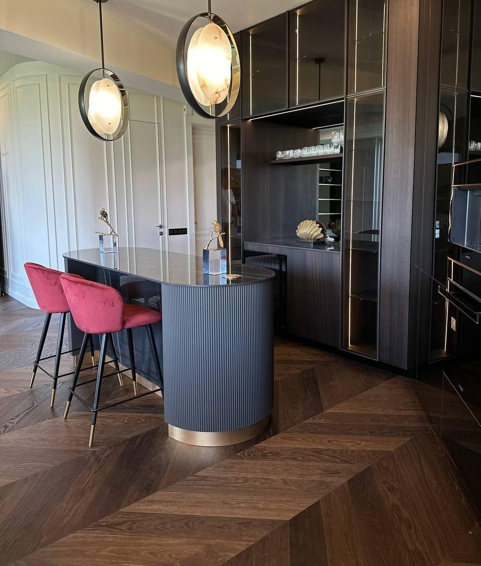 Elegant kitchen with dark wood and French herringbone parquet flooring in smoked oak. Pink velvet chairs add a touch of flair to the room.