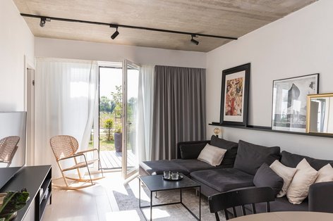 Blick auf ein Wohnzimmer mit Betondecke und schwarzer Lampenleiste, Stuhl aus Wiener Geflecht und Parkettboden