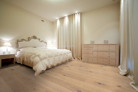 Schlafzimmer mit hellen Farben, weißem Parkett und luxuriösem Bett.