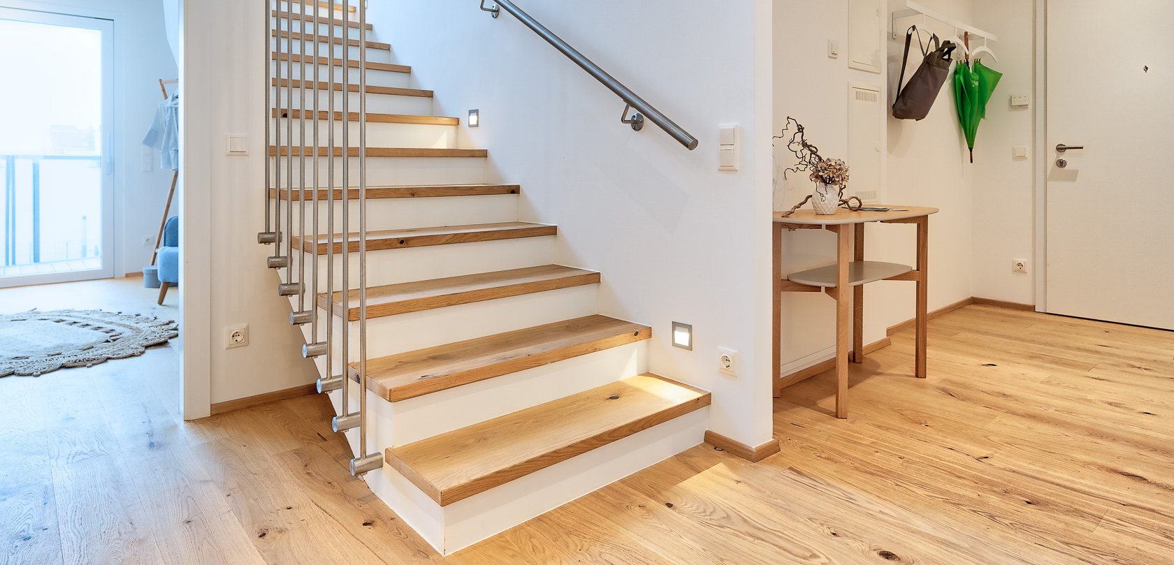 Entrance hall with a lit wooden staircase made of oak, matching the parquet flooring. An open door leads to the bedroom.