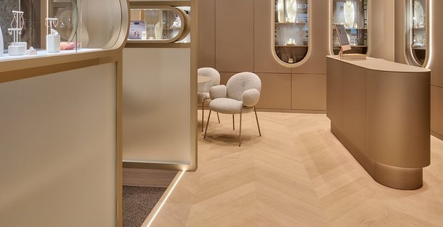 [Translate to EN:] Uhrenboutique mit luxuriösem Interior in Creme und Gold. Am Boden liegt hochwertiges Französisches Fischgrät Parkett in weiß geölter Eiche.