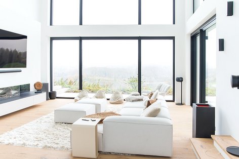 View of a modern living room and the outdoors through large windows. The room is decorated in black and white and has a wooden floor