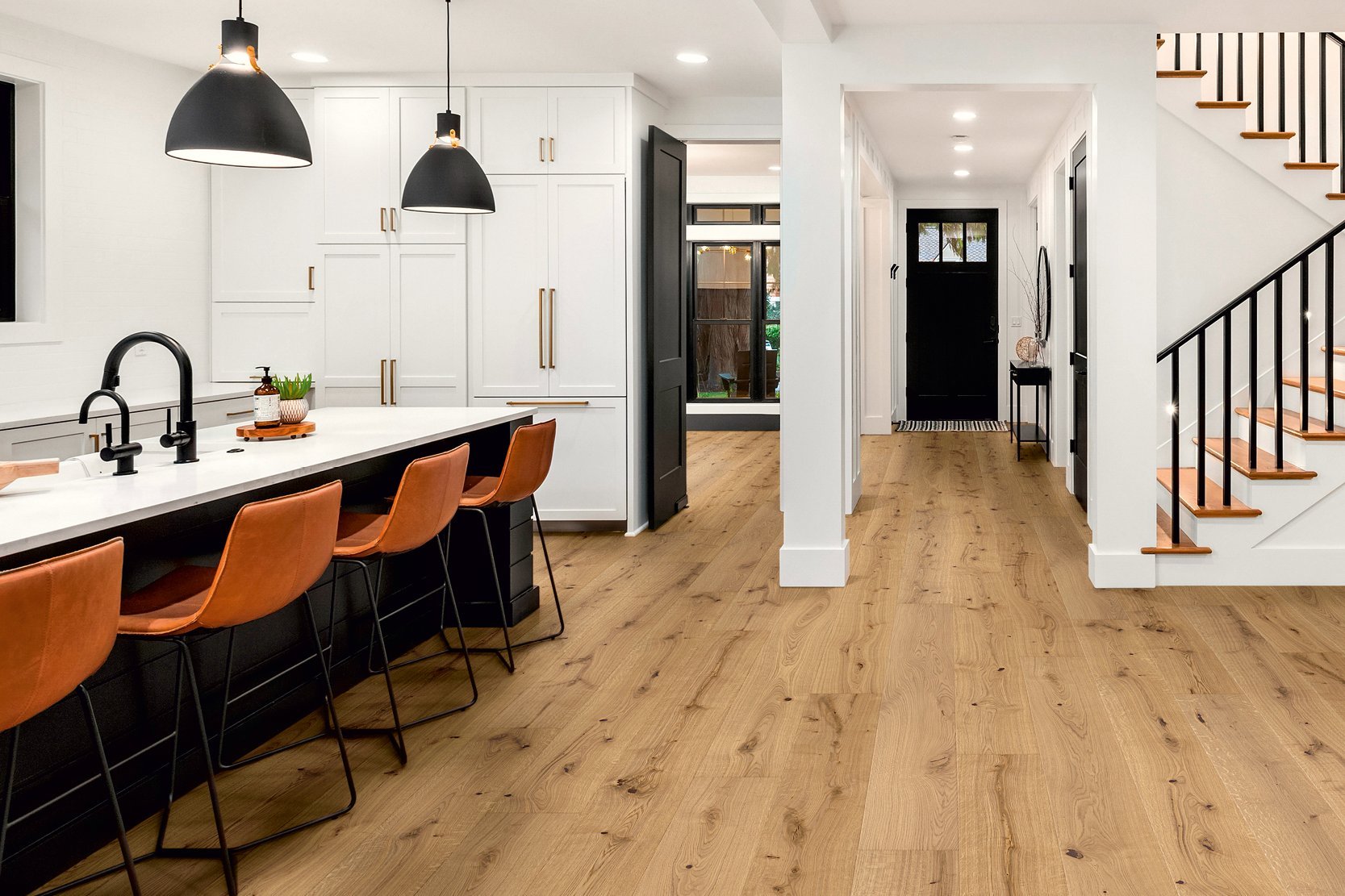 Black American-style kitchen unit, brown bar stools combined with oak parquet flooring and staircase that stylishly complements the room