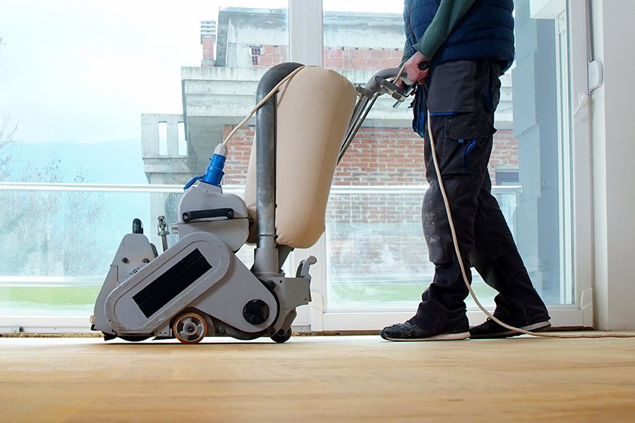 Parkettboden wird von einem Mann mit SChleifmaschine abgeschliffen