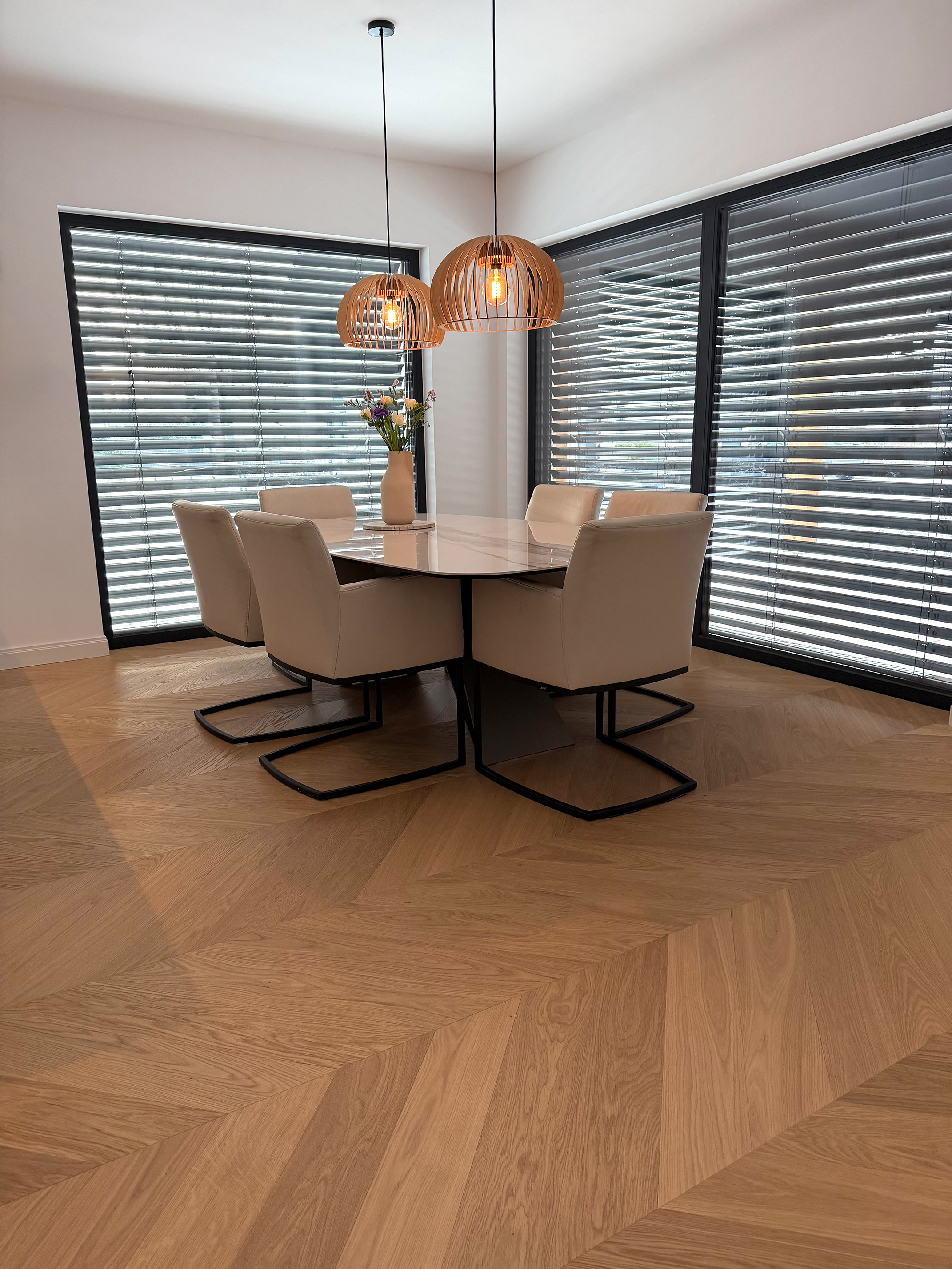 Modernes Esszimmer mit Französisch Fischgrät Parkett in weißlicher Eiche, schwarzen bodentiefen Fenstern und beigen Ledersesseln