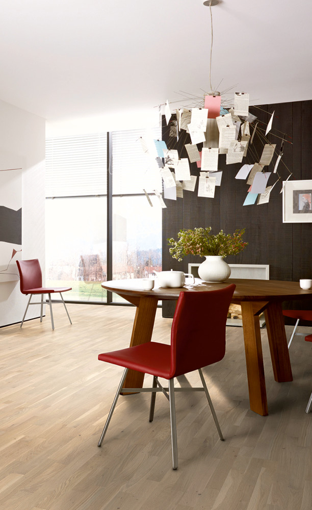 Esszimmer mit moderner Händeleuchte mit Karten. Im Raum ist ein Schiffsboden in Eiche verlegt und eine schwarze Rückwand lässt rote Stühle und den Holztisch besonders gut zur Geltung kommen.