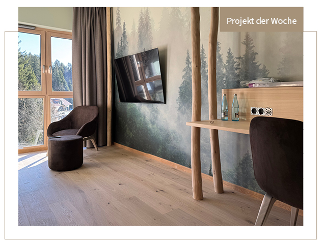 Hotelzimmer mit gräulichem Parkettboden, Holzmöbeln, Waldtapete und Fernseher an der Wand.