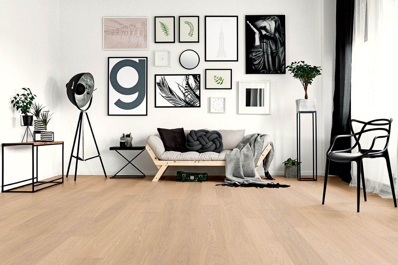 Modern, industrial-style living room with white oiled parquet flooring. The furniture is in shades of gray and black, and numerous pictures in black frames hang on the wall.